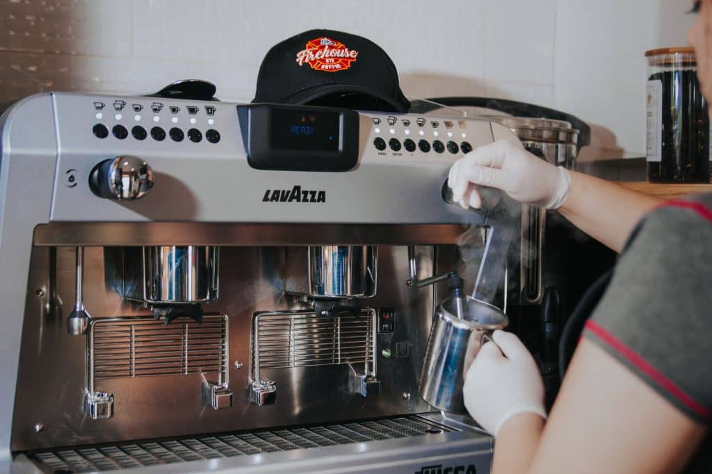 lavazza koffiebonen — Barista steaming milk with Lavazza espresso machine, indoors, wearing gloves.
